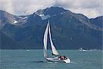 Menschen, die in der Resurrection Bay in der Nähe von Seward mit Kenai Mountains im Hintergrund, South Central Alaska, Sommer Segeln