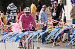 Senior man dressed in a pink shirt and tutu costume bikes across the finish line during the Pink Cheeks Triathlon, Seward, Southcentral Alaska, Summer