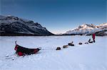 National Park Ranger rests with his dog team on the North Fork of the Koyukuk River at sunset with the Gates of the Arctic in the background, Brooks Range, Arctic Alaska, Winter