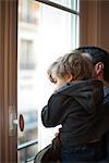 Toddler boy in father's arms, looking out window