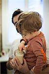 Toddler boy in father's arms, testing temperature of milk in baby bottle
