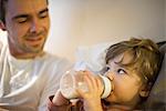Toddler boy with father, drinking milk from baby bottle