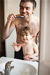 Father and toddler son brushing their teeth together