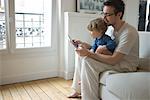 Toddler boy watching father using digital tablet