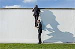 Businessman lifting colleague over wall