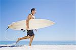 Homme transportant planche de surf sur la plage