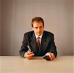 Annoyed businessman sitting at desk holding mobile phone
