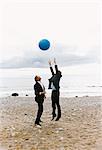 Two businessmen in suits playing with ball in beach