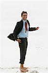 Barefoot businessman standing on rock in sea, laughing