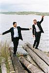 Zwei lächelnde Geschäftsleute in Anzügen balancieren auf Treibholz am Ufer