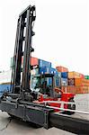 Red forklift truck with pile of big metal goods containers