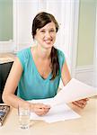 Smiling woman sitting at desk holding papers