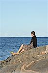 Woman sitting by the sea, Vaddo, Stockholm archipelago, Sweden.