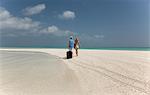 Couple rolling luggage on beach