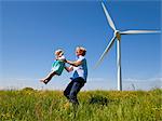 Man in daughter in field by wind turbine
