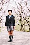 High School Girl Standing On Pathway With Cherry Blossoms In Background