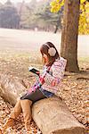 Japanese Women Sitting On Ginkgo Tree-Trunk And Reading Book