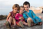 Jeunes frères et sœurs assis sur une plage rocheuse, portrait