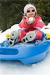 Toddler girl on sled, snowball in hands