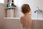 Toddler standing by bathtub playing, rear view
