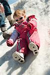 Toddler girl in snow-suit sitting on snow