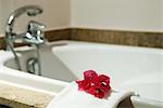 Fresh towel decorated with flower heads handing on edge of bathtub