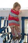 Toddler girl standing on chair, peeking over balcony railing, rear view