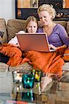 Mother and daughter using a laptop in a couch, Sweden.