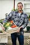 Homme portant une boîte pleine de légumes.