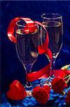 two glasses of champagne, red twisted ribbon, carnation and plastic heart on the blue velvet