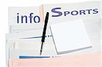 Note and pen, over stacked sports newspapers on white background