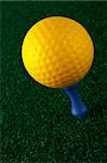 Yellow golfball and blue tee on grass background