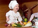 laughing little boy in the cook costume at the kitchen with vegetables