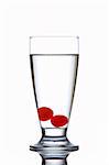 Glass of fresh water with cherries reflected on white background