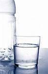 Detail of bottle and glass of mineral water with droplets reflected on white background