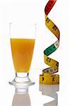 A glass of fresh orange juice and tape measure reflected on white background