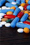 Collection of assorted pills on a dark wood table. Shallow depth-of-field.