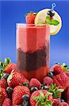 A glass of layered berry smoothie surrounded by fresh fruits (strawberry,raspberry,blueberry)