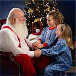Santa Claus talking with two young girls in pajamas, christmas decorations in background, indoor studio shot, square format, focus on foreground