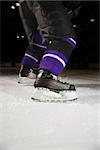 Low angle of hockey player's legs and skates on ice rink.