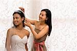 Asian bridesmaid adjusting veil of African-American bride.