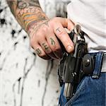 Caucasian tattooed man wearing holster with gun.