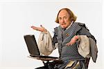 William Shakespeare in period clothing sitting in school desk with laptop computer shrugging at viewer.