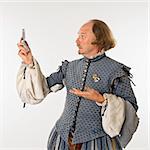 William Shakespeare in period clothing looking at cell phone with astonishment.