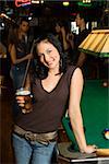 Portrait of young caucasian woman holding beer beside billiards table in pub.