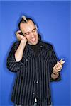 Caucasian man smiling with mohawk listening to headphones holding cd standing against blue background.