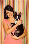 Young adult female Caucasian holding Boston Terrier dog on striped background.