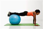 Profile of African American woman doing push ups with feet on exercise ball.