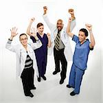 Full-length portrait of African-American man and Caucasian women medical healthcare workers in uniforms cheering with arms raised standing against white background.