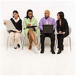 Multi-ethnic business group of men and women sitting looking at laptop and papers.